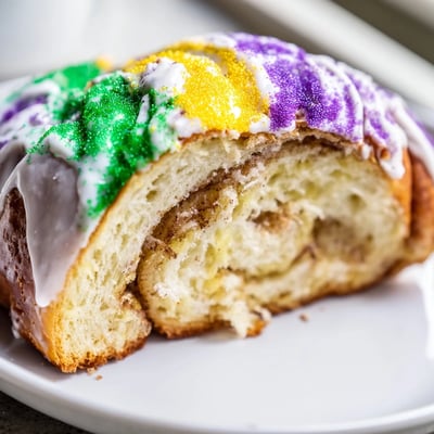 Golden-brown Mardi Gras King Cake on a platter, revealing a cinnamon sugar swirl inside, perfect for a traditional New Orleans Mardi Gras party.